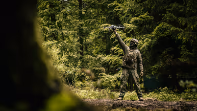Een militair laat een drone opstijgen in het bos.