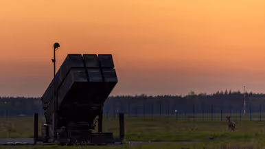 Op de linkerfoto een NASAMS-lanceerinrichting in het avondrood. Op de rechterfoto monteren militairen stabilisatievinnen op een luchtdoelraket.