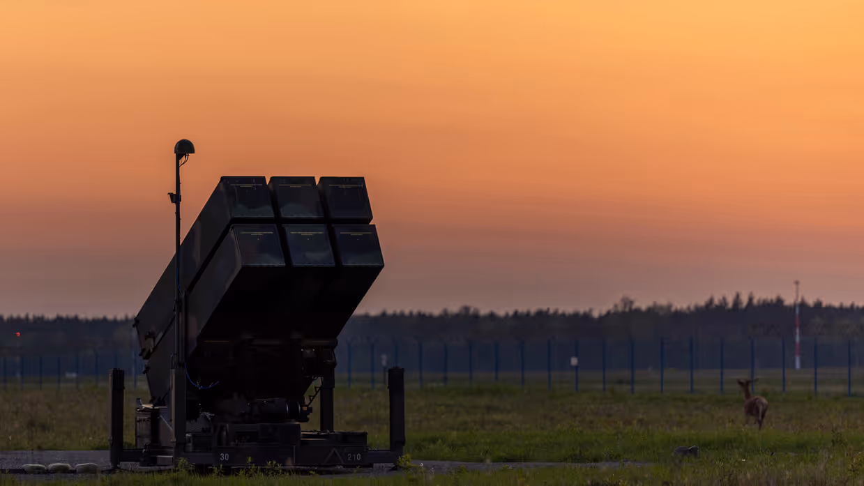 Op de linkerfoto een NASAMS-lanceerinrichting in het avondrood. Op de rechterfoto monteren militairen stabilisatievinnen op een luchtdoelraket.