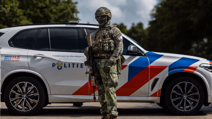 Militair staat voor een politiewagen in een bosrijke omgeving.