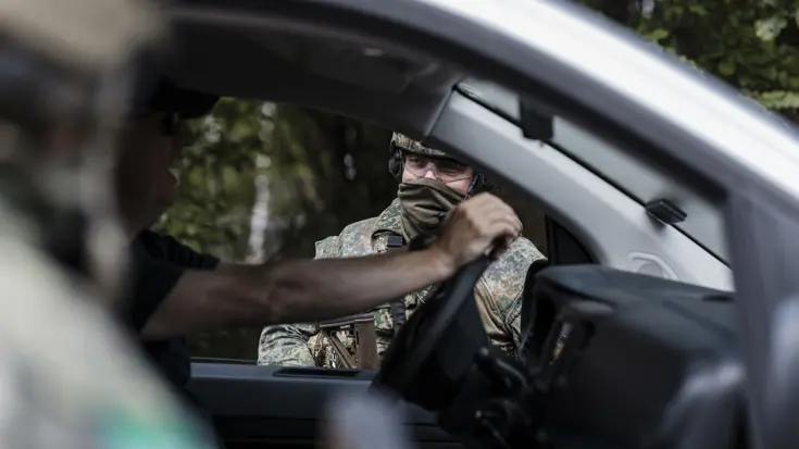 Een man in een voertuig, waar een militair een gesprek mee voert door het voorraam van dit voertuig.