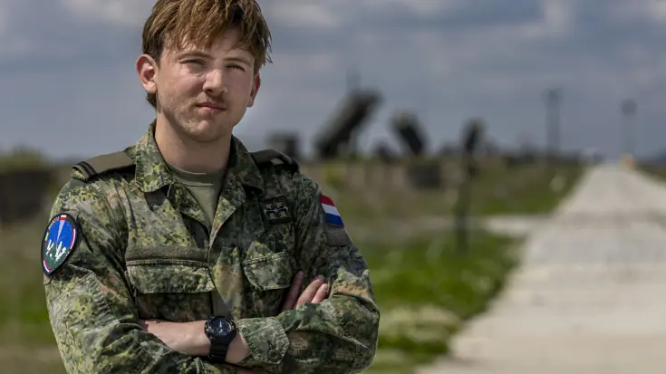 Ronan staat met de armen over elkaar. Op de achtergrond staan Patriot-lanceerinstallaties.