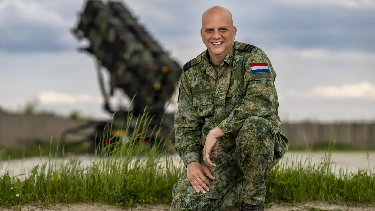 Maurice zit gehurkt op één knie. Op de achtergrond staat een Patriot-lanceerinrichting.