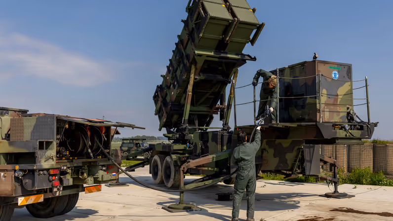 Twee militairen tillen een brandstofslang naar een aggregaat op een lanceerinstallatie.