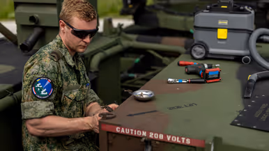 Op de linkerfoto sleutelt een militair aan een wapensysteem. Op de rechterfoto een mouwembleem van de AMDTF.