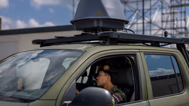 Twee militairen zitten in een voertuig met een grijze bol op het dak. 