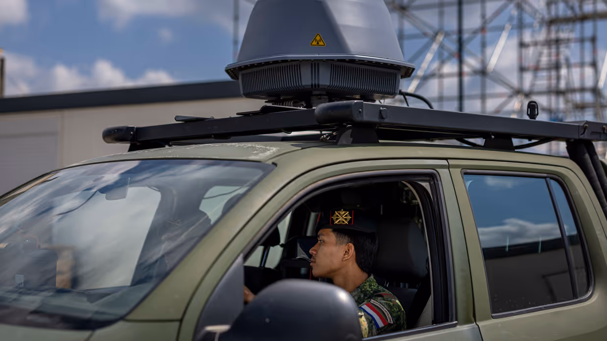 Twee militairen zitten in een voertuig met een grijze bol op het dak. 