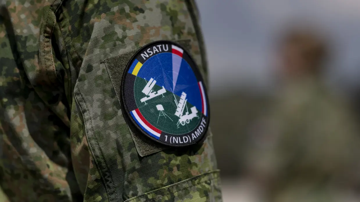 Op de linkerfoto sleutelt een militair aan een wapensysteem. Op de rechterfoto een mouwembleem van de AMDTF.