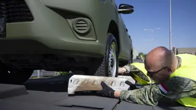 Op de linkerfoto ene kleine file van legervoertuigen op een rangeerterrein. Op de rechterfoto plaatst een militair een blok bij de voorwielen van ene voertuig.