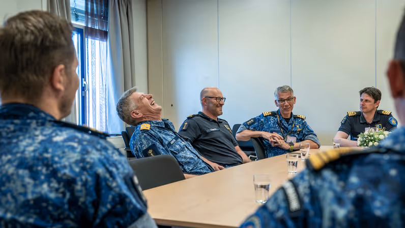  6 marinemensen zitten lachend met elkaar aan een tafel.