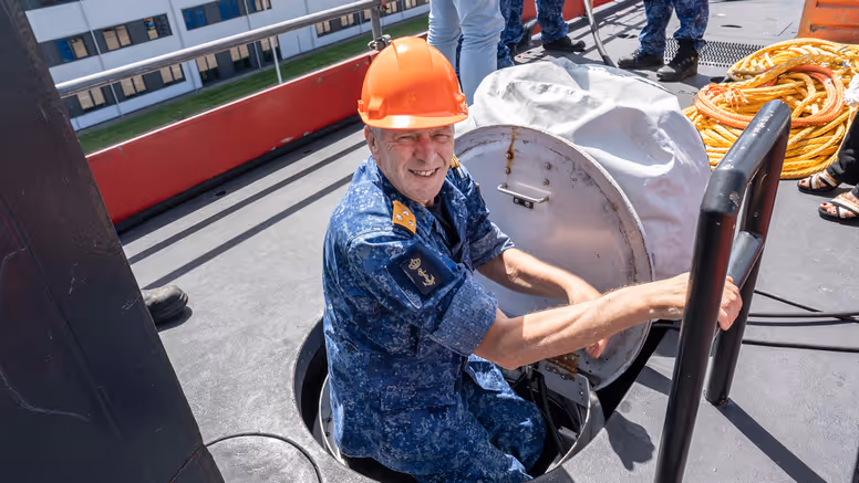 Een viceadmiraal met oranje bouwhelm klimt uit een onderzeeboot. 