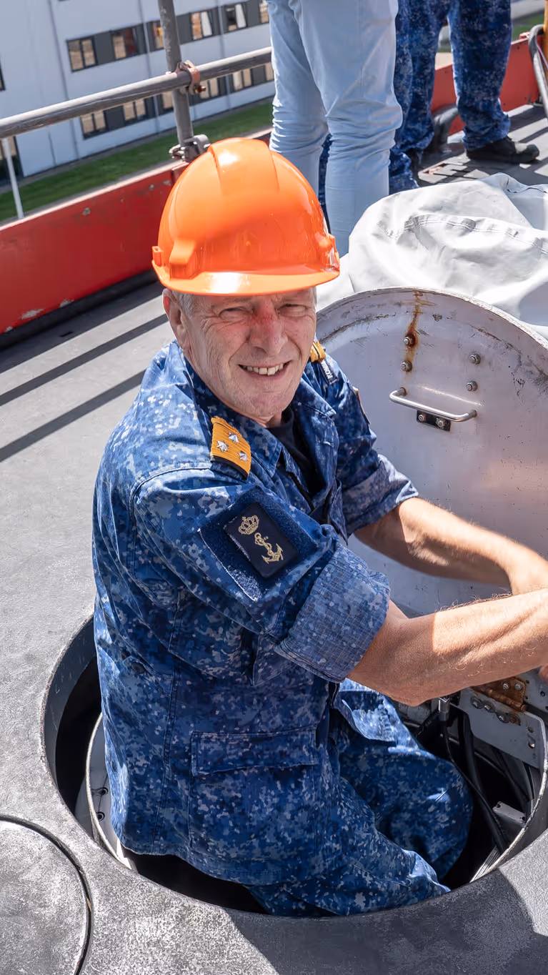Een viceadmiraal met oranje bouwhelm klimt uit een onderzeeboot. 
