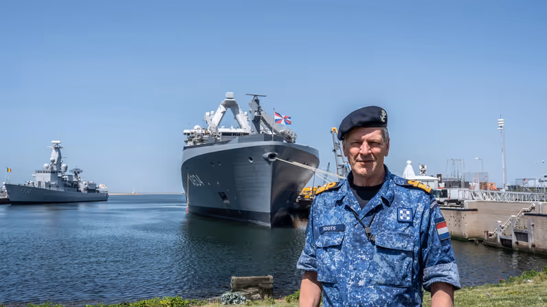 Vice-admiraal Boudewijn Boots poseert met baret op in de haven voor een marineschip. 