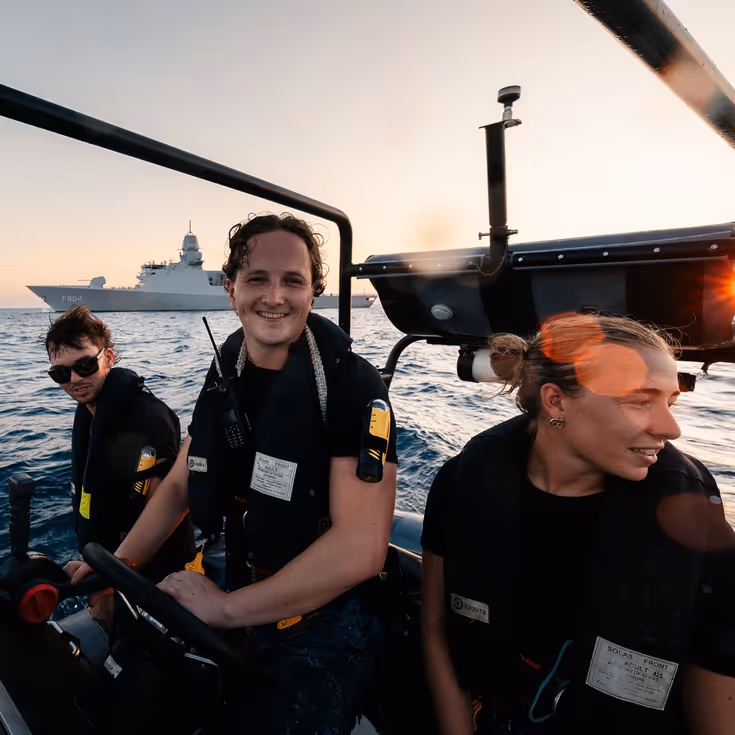 3 marinemensen varen met een RHIB, op de achtergrond ligt Zr.Ms. De Ruyter op zee.