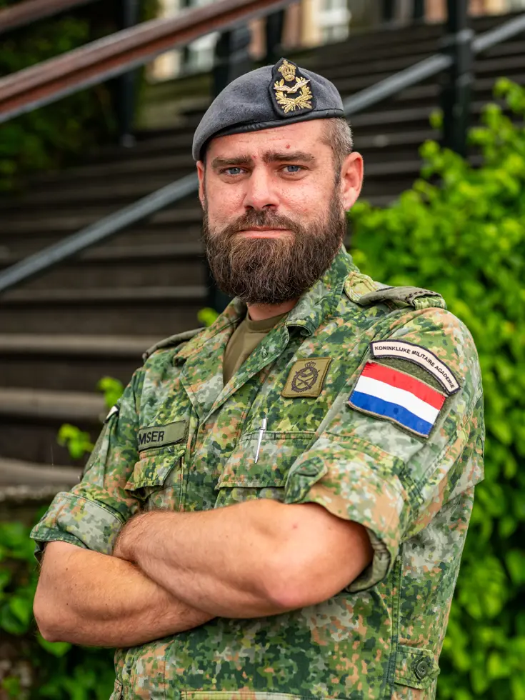 Tim Gramser in actie als instructeur, sprekend met cadetten en portretterend voor de foto, terwijl hij in de camera kijkt en een groen vlekkenpak draagt.  
