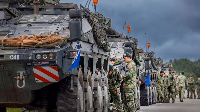 Militaire voertuigen staan opgesteld terwijl militairen zich voorbereiden op vertrek. 