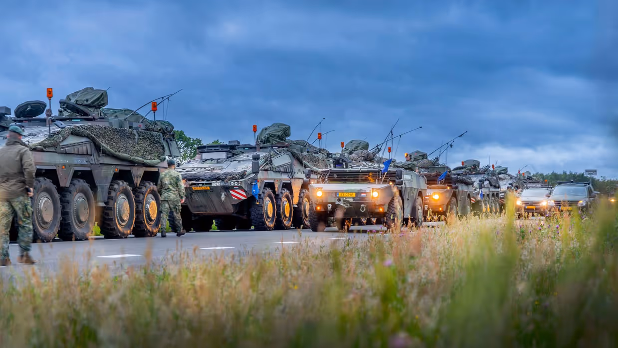 Militaire voertuigen staan opgesteld langs een weg onder een donkere lucht. 