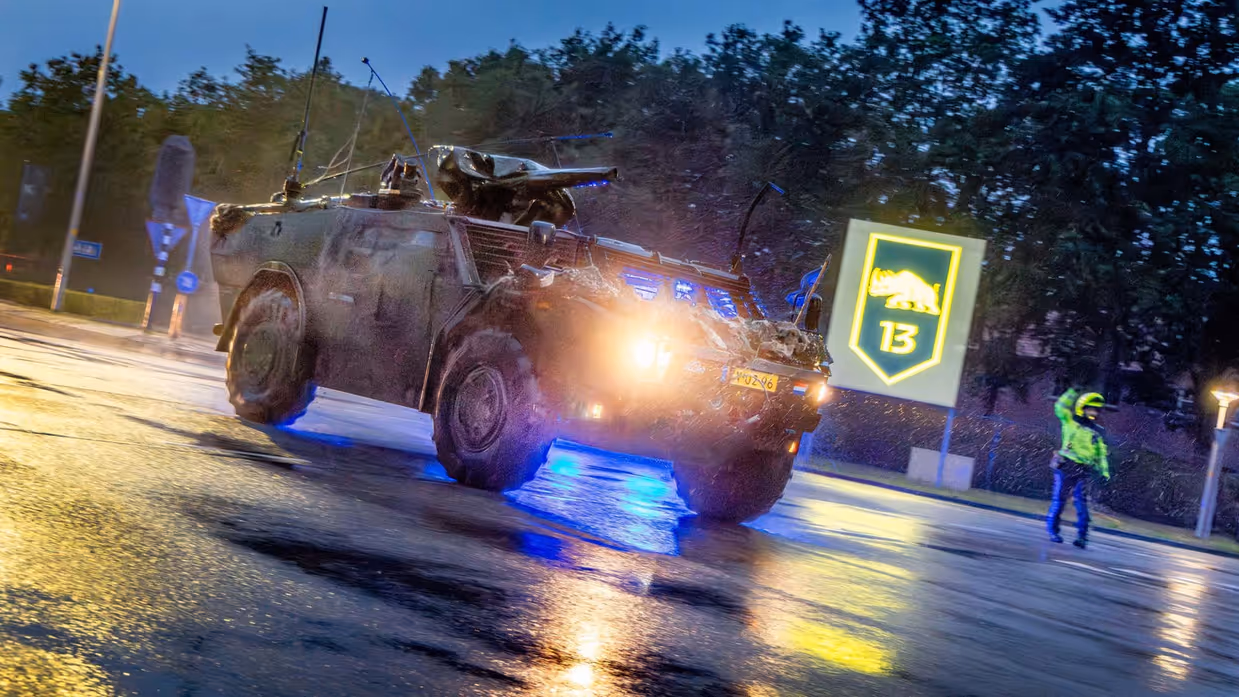 Een militair voertuig van 13 Lichte Brigade rijdt in de regen de kazerne uit bij vertrek naar oefening Fighter Lion.