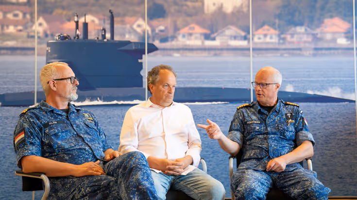 3 mannen van wie de buitenste 2 in marine-uniform praten met elkaar voor poster onderzeeboot.