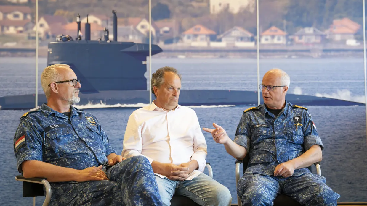 3 mannen van wie de buitenste 2 in marine-uniform praten met elkaar voor poster onderzeeboot.