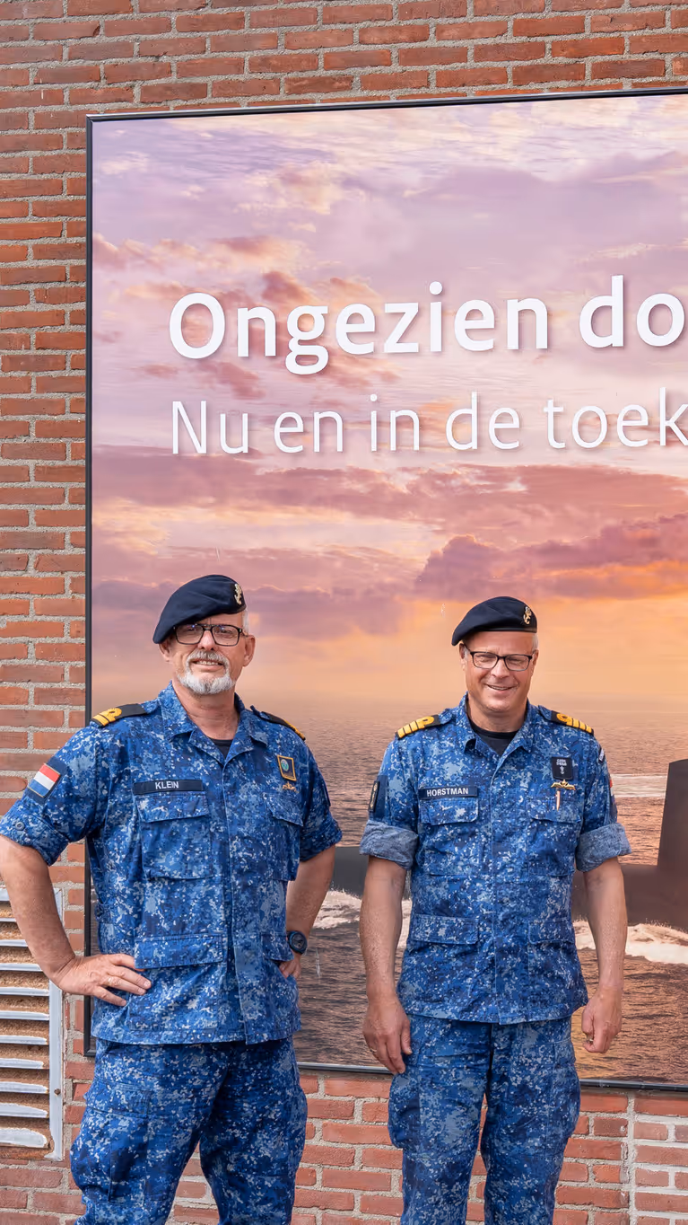 2 marinemannen poseren in uniform voor een billboard van de Onderzeedienst.