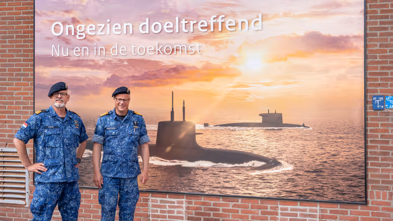 2 marinemannen poseren in uniform voor een billboard van de Onderzeedienst.