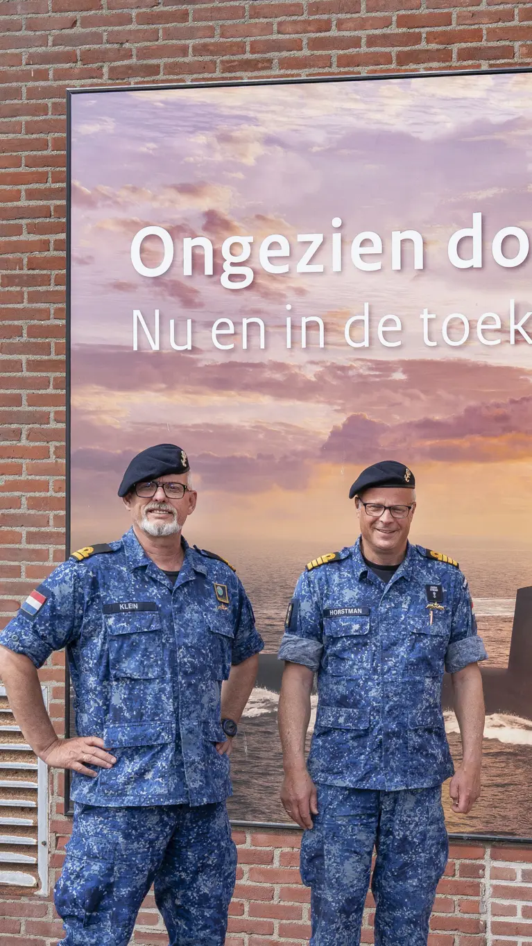 2 marinemannen poseren in uniform voor een billboard van de Onderzeedienst.