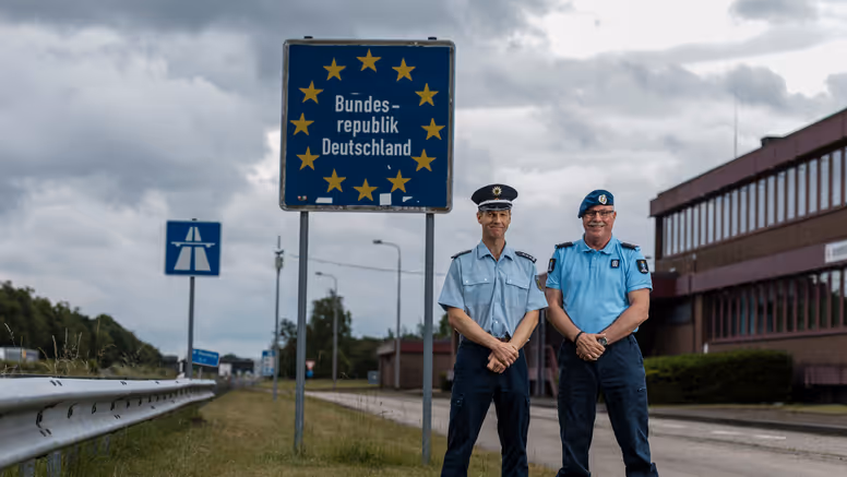 Eerste luitenant Herman en zijn Duitse evenknie voor een grensbord langs de snelweg. 