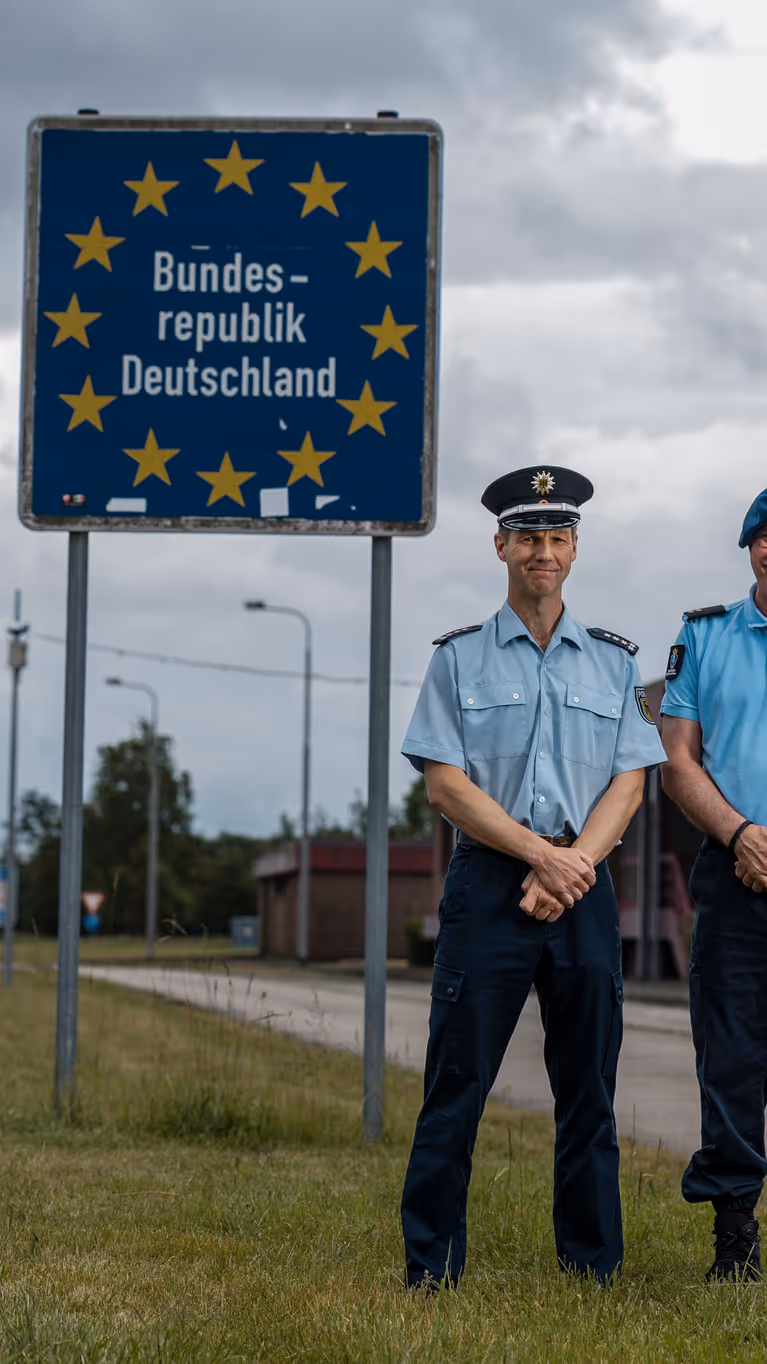 Eerste luitenant Herman en zijn Duitse evenknie voor een grensbord langs de snelweg. 