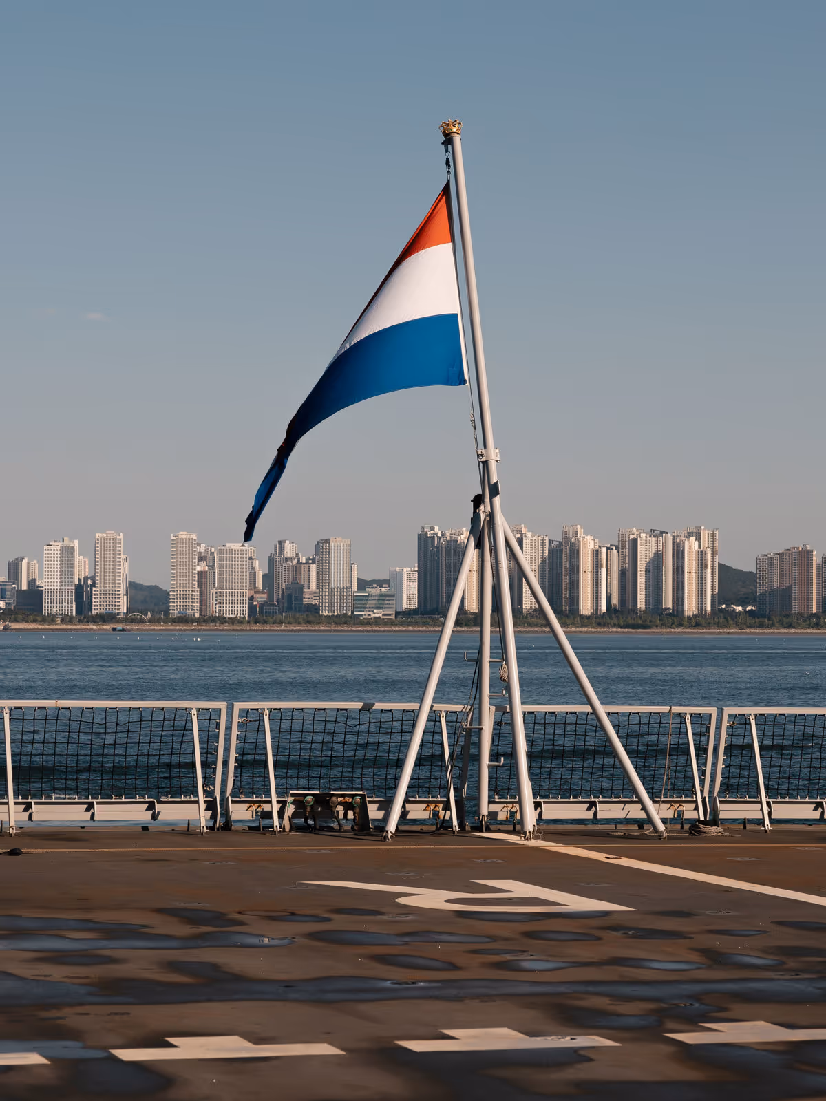 Nederlandse vlag op dek van schip met uitzicht op wolkenkrabbers.