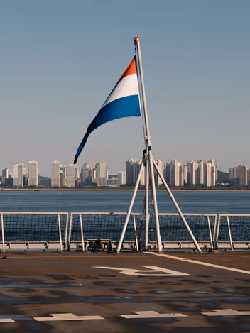 Nederlandse vlag op dek van schip met uitzicht op wolkenkrabbers.