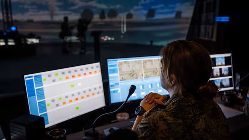 Een vrouwelijke militair kijkt over haar schermen naar de ruimte waarin de Stingerschutters rondlopen.