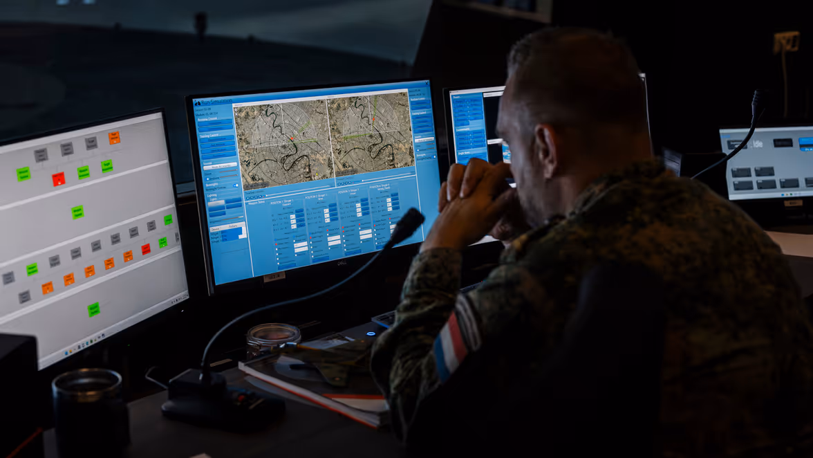 Een mannelijke militair in gevechtspak tuurt naar de schermen voor zijn neus.