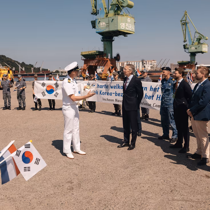 De commandant van de De Ruyter is de wal opgegaan en wordt hartelijk ontvangen door een grote delegatie met een spandoek en Koreaanse vlaggetjes.