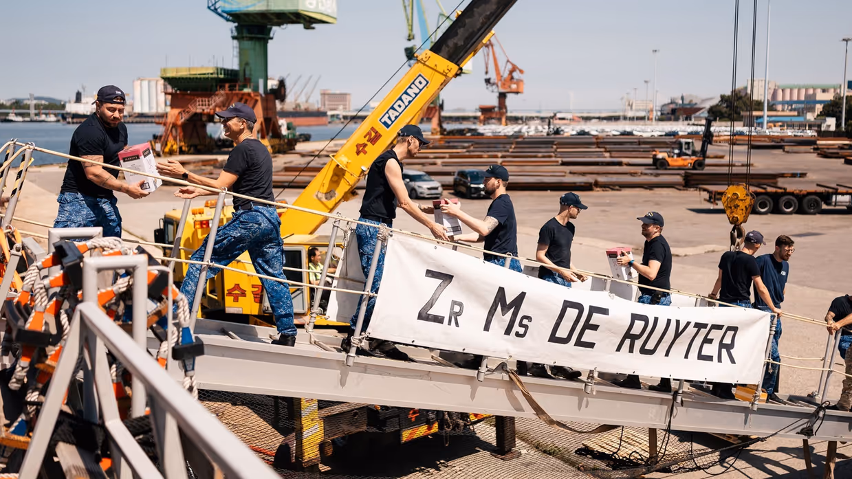 Bemanningsleden vormen een keten op de valreep en geven dozen aan elkaar door.