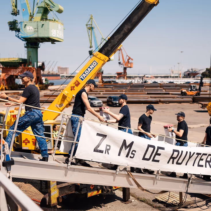Bemanningsleden vormen een keten op de valreep en geven dozen aan elkaar door.