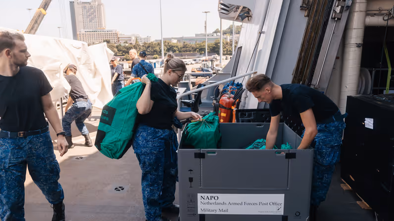 2 marinemensen snuffelen op dek marineschip in een kist met postzakken.