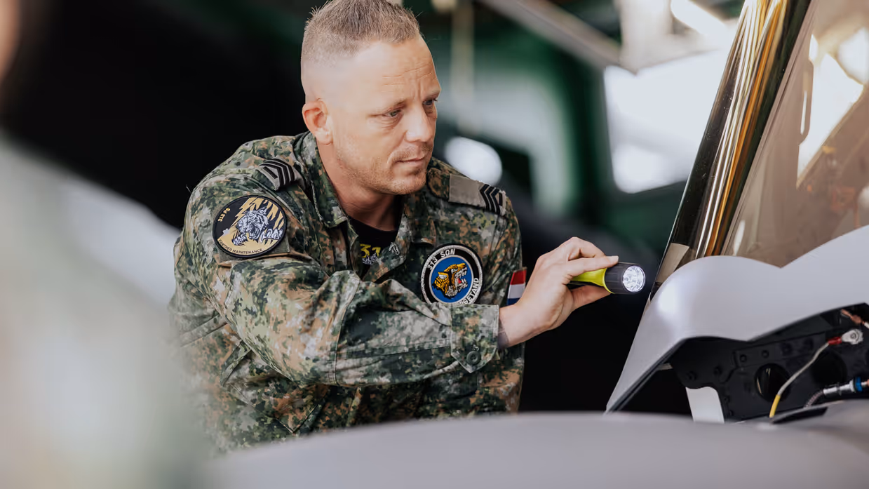 Glenn Afman in groen vlekkenpak inspecteert van dichtbij met een zaklamp een F-35. 