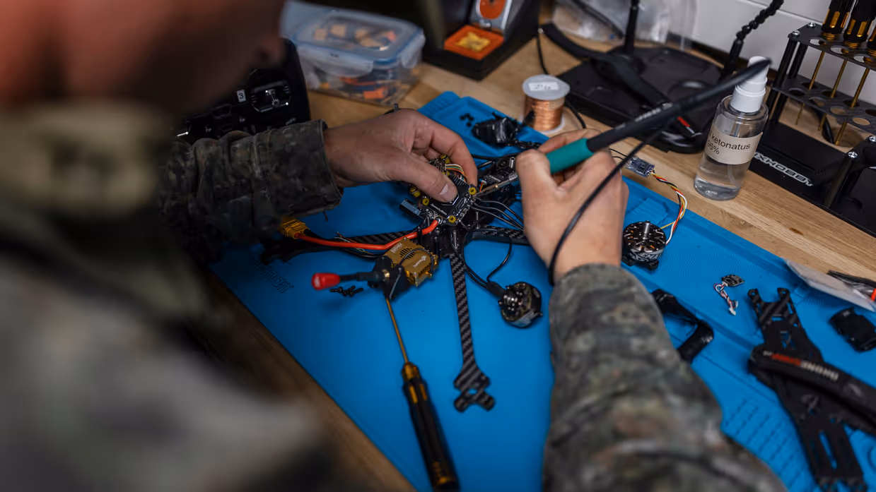 Een militair soldeert een drone op een werkbank in de mobiele werkplaats van TechDevOps tijdens oefening Fighter Lion.