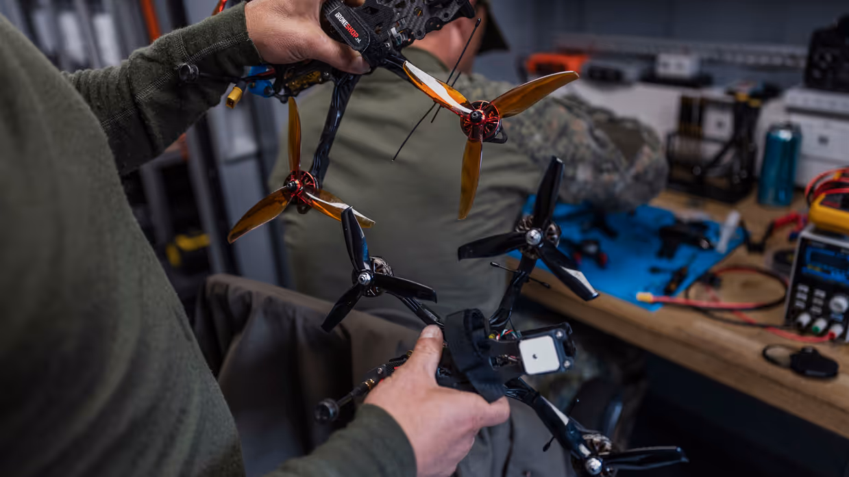 Militairen vergelijken twee drones in de mobiele werkplaats van TechDevOps tijdens oefening Fighter Lion.