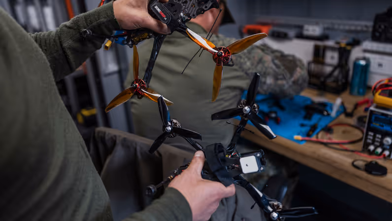 Militairen vergelijken twee drones in de mobiele werkplaats van TechDevOps tijdens oefening Fighter Lion.