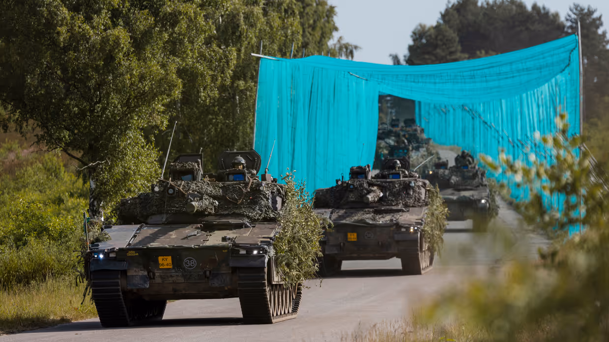 Leopard 2A8-gevechtstanks rijden tijdens oefening Fighter Lion onder camouflagenetten door over een bosweg.