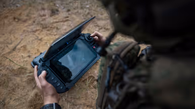 Een militair bedient tijdens oefening Fighter Lion de grondcontroller van een drone en bekijkt de livebeelden op het scherm.