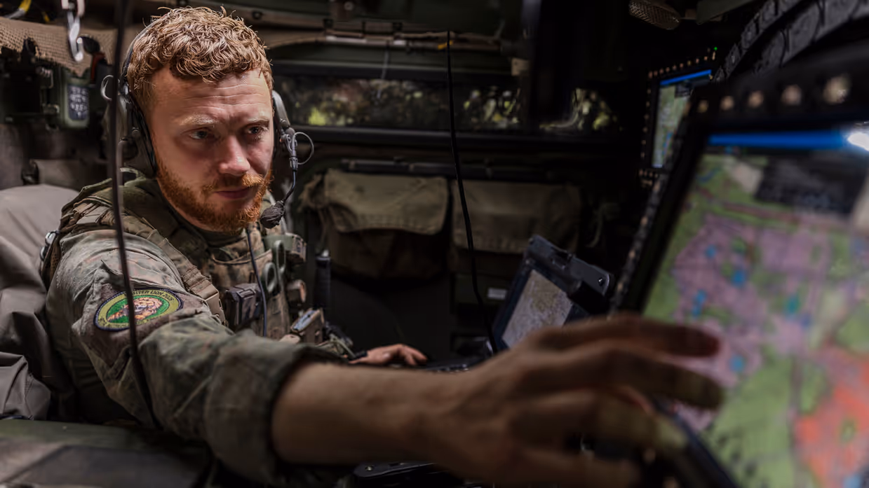 Een Forward Observer werkt in een commandovoertuig achter digitale schermen en beoordeelt meldingen van het AITAS-systeem.