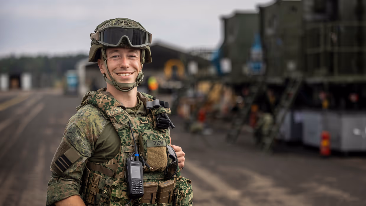 Militair met vest en helm op staat op taxibaan vliegbasis.
