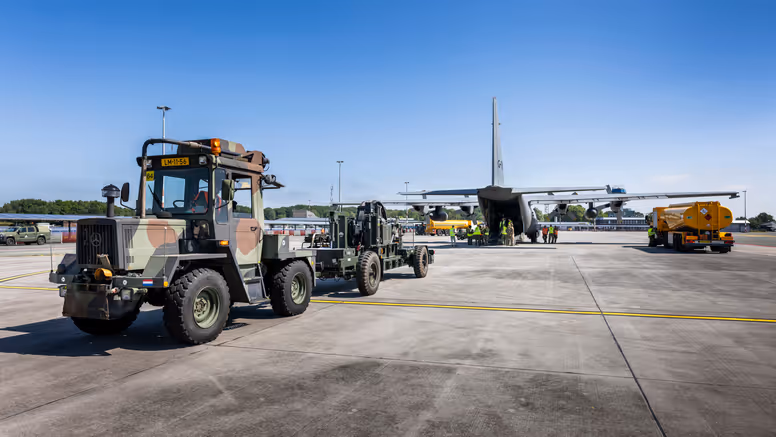 Truck en oplegger staan op een vliegveld klaar met materieel om Hercules-transportvliegtuig in te laden.
