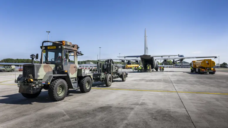 Truck en oplegger staan op een vliegveld klaar met materieel om Hercules-transportvliegtuig in te laden.