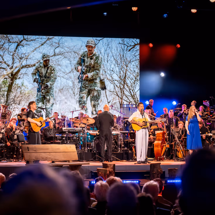 Drie solisten spelen en zingen op het podium. In de achtergrond het orkest van de luchtmacht.