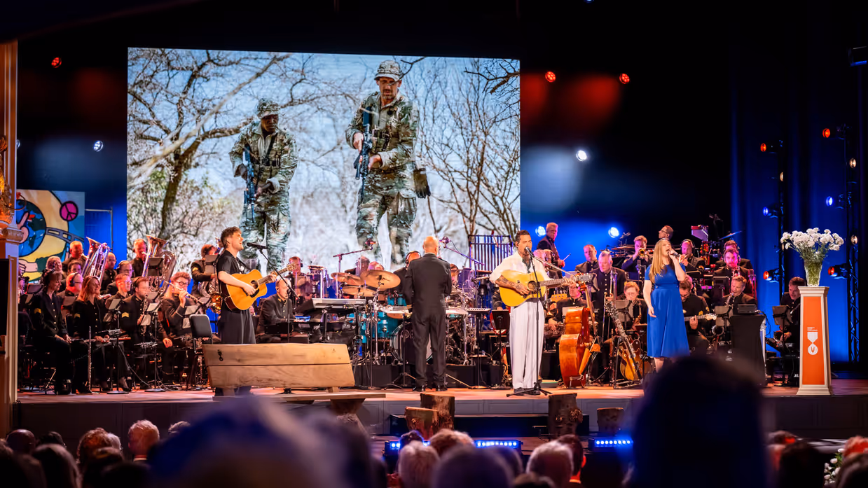 Drie solisten spelen en zingen op het podium. In de achtergrond het orkest van de luchtmacht.