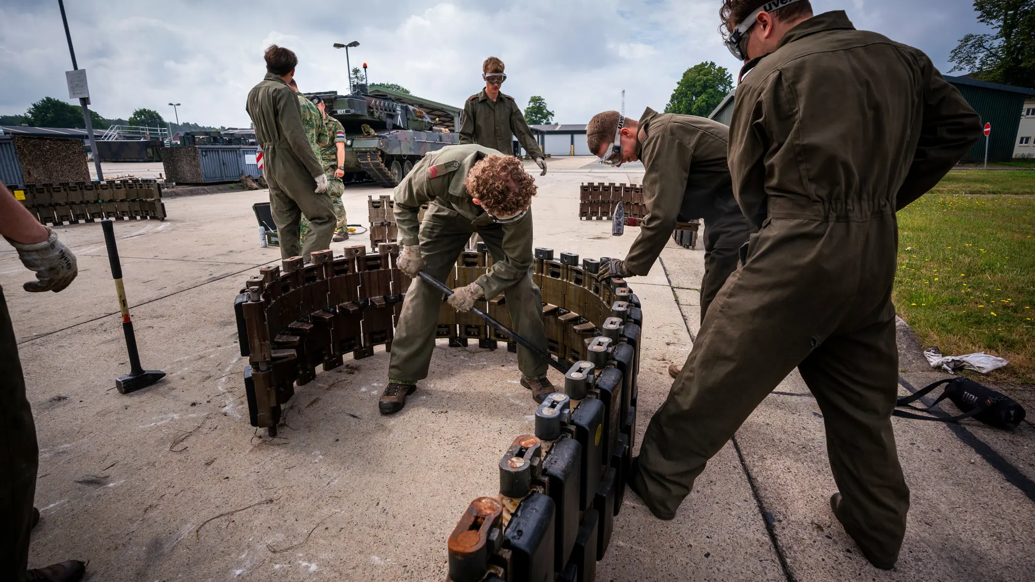 Een groep soldaten in groene overall werkt samen aan het monteren van een zware, metalen structuur in een buitenomgeving.